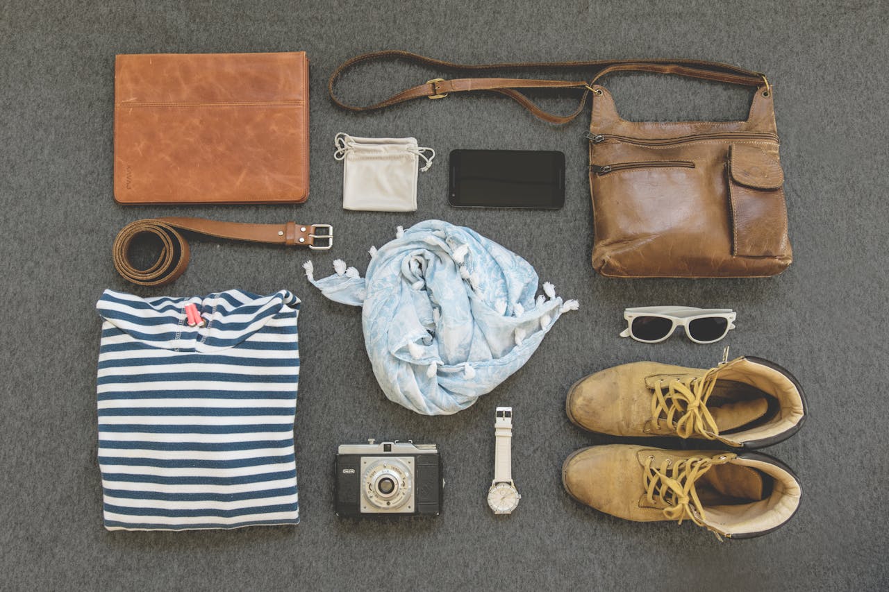 our-story Vintage travel essentials flat lay with leather bags, shoes, camera, and clothing.